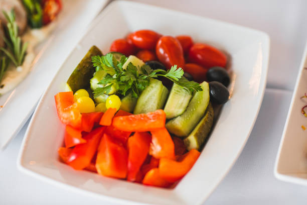 Deep white plate with various vegetables cucumber, cherry, pepper stands on buffet table in restaurant. Vegetarian food. Fresh food. Dietetics. Enjoying taste. Healthy lifestyle.
