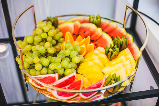 Round dish with variety of fresh organic fruits on buffet table at festive event. Mini snacks and treats. Conducting special events and parties. Enjoying life and taste. Restaurant business.