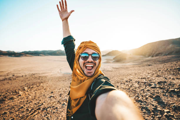 istock Happy traveler with backpack taking selfie picture with smart mobile phone outdoors - Cheerful guy smiling on the top of the mountain - Hiker traveling in rocky desert - Travel technology life style 1982249900