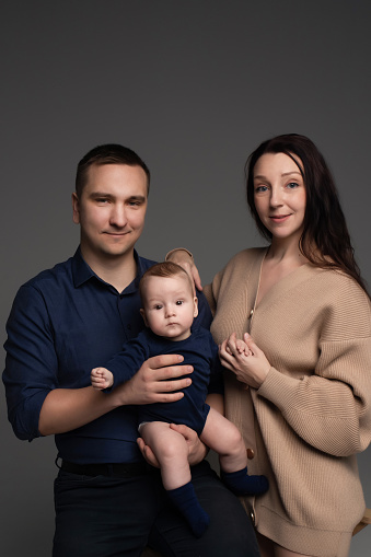 close-up portrait of happy parents looking into the frame with their little son in their arms. family posing for a minimalistic photograph on a dark background. father and mother with little son.