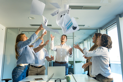 Happy and smiling businesspeople throwing paperwork in the air, celebrating success and working in the modern office.