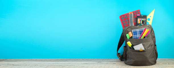istock Backpack with different colorful stationery on table. Blue background. Back to school. Banner design. 1982308111