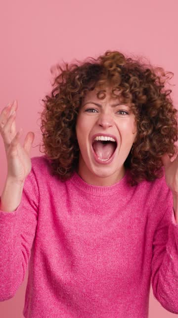 Shocked young woman showing stretched hands with palms on pink background. Vertical footage