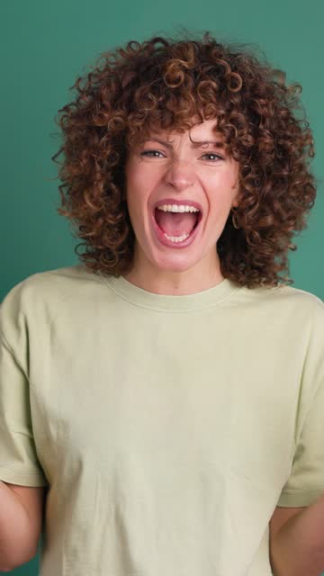 Shocked young woman showing stretched hands with palms on green background. Vertical orientation