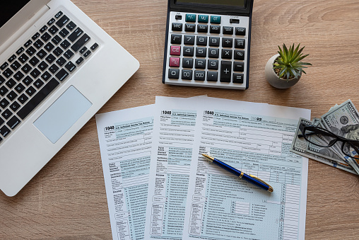 Tax Season 1040 individual tax form with with laptop and pen, dollar bills on office desk.  Deadline paperwork concept