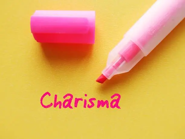 Photo of Pink highlight pen on yellow background with handwritten text CHARISMA, refers to people who have naturally ability to influence others, attract attention and admiration