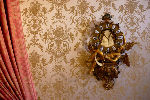 Ornate wall clock in front of wallpaper and a red curtain. Taken in the Residenz in Wurzburg, Germany.