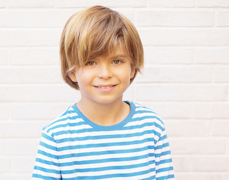 Frontal portrait of a 9-year-old blond-haired green-eyed boy smiling at the camera. Isolated on white background. Horizontal.
