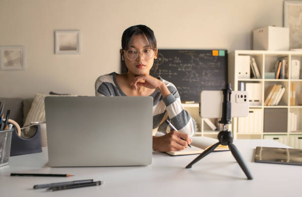 istock Young Asian teacher transforms her living space into an engaging online classroom,  teaching online with passion, concept of online teaching and education. 1982476860