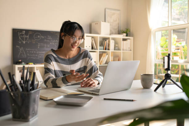 istock Young Asian teacher transforms her living space into an engaging online classroom,  teaching online with passion, concept of online teaching and education. 1982476861