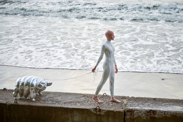 Hairless girl with alopecia in futuristic suit walking with toy tardigrade on sea background Young hairless girl with alopecia in white futuristic suit walking on concrete fence with toy tardigrade on sea background, bald pretty girl symbolizes courage and acceptance of unique appearance water bear stock pictures, royalty-free photos & images