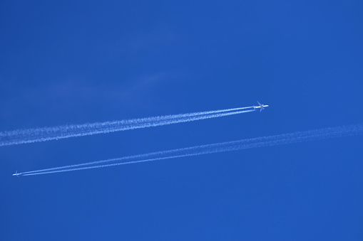 Two airplanes in the blue sky with contrails, closeup of photo