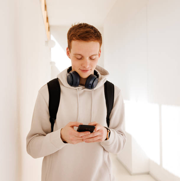 istock Male student with ginger hair walking in the corridor and using mobile phone 1982514821