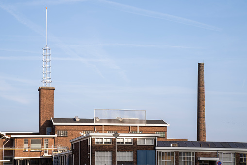 View of a factory chimney with smoke coming out behind a red roof with the sky in the background