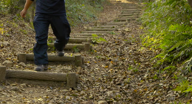 A man walking on a mountain trail covered with brown fallen leaves