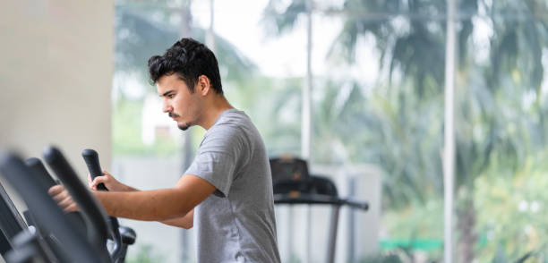 Determined man using an elliptical trainer for cardio workout in a gym stock photo