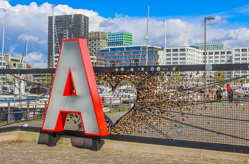 Antwerp, Belgium - April 2022: a red letter ‘A’ places near the ‘Museum aan de Stroom’, which is a museum on the river Scheldt located in Antwerp, Belgium's most populous city and the capital of the Antwerp province, in Flanders. Behind the  A for Antwerp Sign is ‘Mr Lovelock’  (Liefdesslotjeshekwerk), a chainlink fence with love locks.