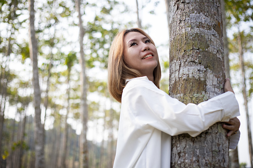 Happy Asian lady hug tree trunk in outdoor leisure park activity. Concept of environment and ambient nature care. People love planet earth and stop deforestation lifestyle
