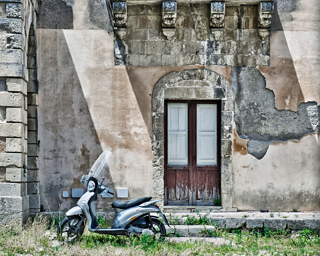 Syracuse, Italy - May 16, 2017:  A scooter parked before a derelict building.