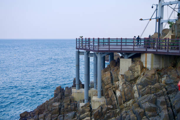 Samcheok City, South Korea - December 28, 2023: The Chogok Yonggul Cave Hiking Trail's walking path, elevated on tall metal supports, traverses the rocky coastline with the East Sea stretching below.