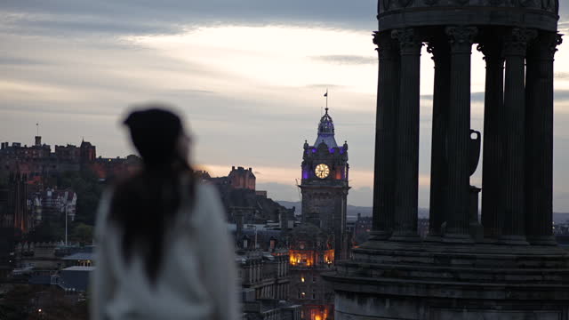 View of Calton Hill, Edinburgh sunset view from calton hill, Gothic Revival architecture in Scotland, View of Edinburgh city center from Calton Hill, Dugald Stewart Monument, Young woman walking on Calton Hill looks around