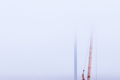 Wind turbine being constructed, obscured by low clouds