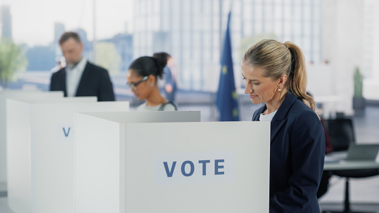 Portrait of a Beautiful Adult Woman Filling Out a Ballot in a Voting Booth on the Day of National Elections in the European Union. Diverse Men and Women Voting for Elected Officials in an EU Country