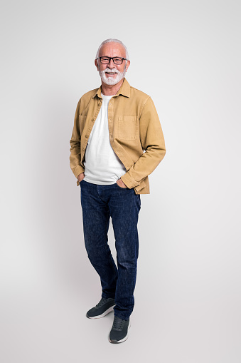 Full length of smiling senior businessman with eyeglasses and hands in pockets on white background