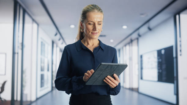 istock Portrait of Caucasian Female Project Manager Using a Tablet Computer and Walking in a Corridor of a Modern Office Building. Successful Businesswoman Working in an International Ecommerce Company 1982627025