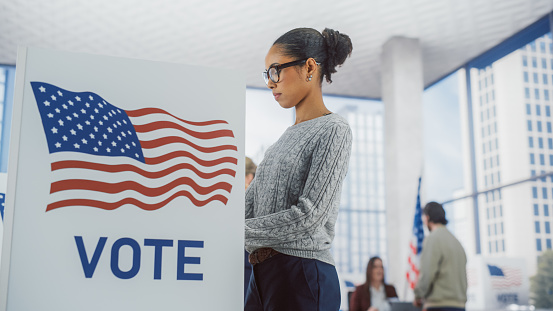 Young Stylish African American Female Casting Her Vote at a Polling Station and Putting Her Ballot into a Sealed Box. American People on Elections Day in the United States of America