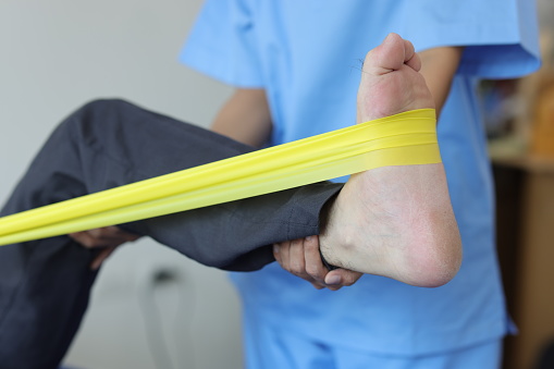 Physiotherapist nurse treating patient with exercise using elastic band therapy rehabilitating man leg. Concept of physical therapy and rehabilitation.