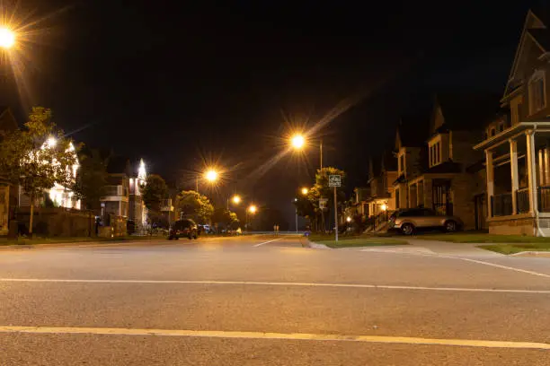 Quiet suburban street at night - illuminated by glowing streetlights - houses lined up - parked cars - clear, starless sky. Taken in Toronto, Canada.