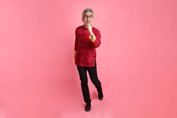 Happy Chinese new year. Asian Chinese energetic senior man wearing red traditional cheongsam qipao or changshan dress with gesture of walking isolated on red background.