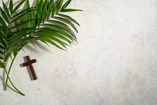 Palm Sunday. Wooden christian cross and palm leaves, top view, copy space. Palm sunday celebration concept.