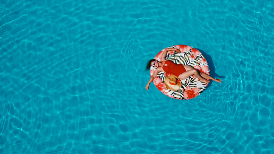 Beautiful Woman in red swimsuit Floating in the pool float in turquoise pool water. Aerial above view. Copy space