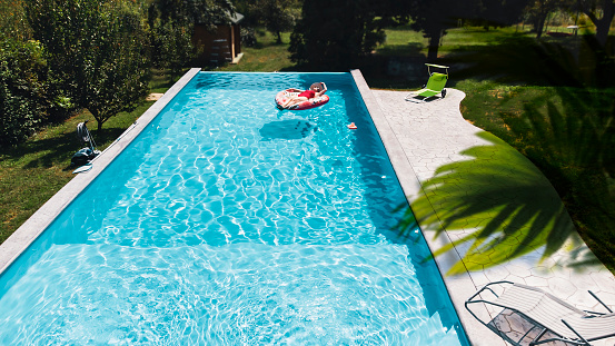 Aerial. Girl resting in a metal frame pool with inflatable toys. Summer leisure and fun concept. Frame pool stand on a green grass lawn. Top view from drone.