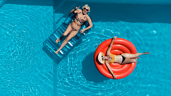 Two Women friends relaxing in the swimming pool on Sunny day. Aerial view directly above