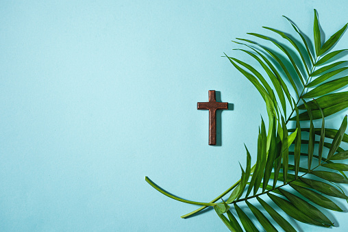 Palm Sunday. Wooden christian cross and palm leaves on blue background, top view, copy space. Palm sunday holiday concept.