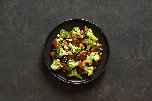 Thinly sliced beef meat with roasted broccoli. Beef with broccoli on black plate over dark stone background with copy space. Top view, flat lay