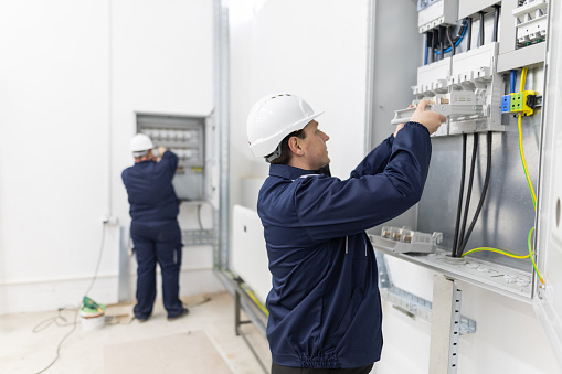 Two male electricians working in an electrical system control cabinet