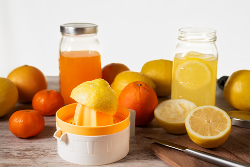 Manual juicer next to several citrus fruits to make juice, next to two jars, one with orange juice and the other with lemon juice.