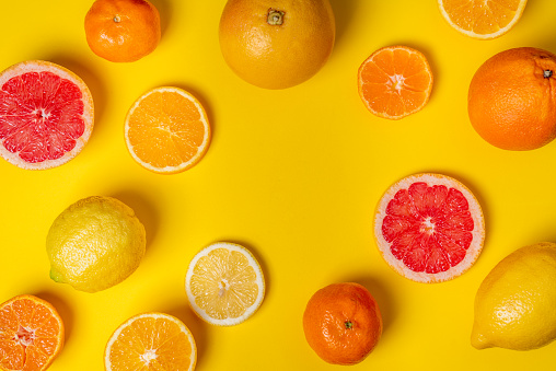 Collage of citrus fruits, whole, half and sliced, grapefruits, oranges, lemons and tangerines, on a yellow background.