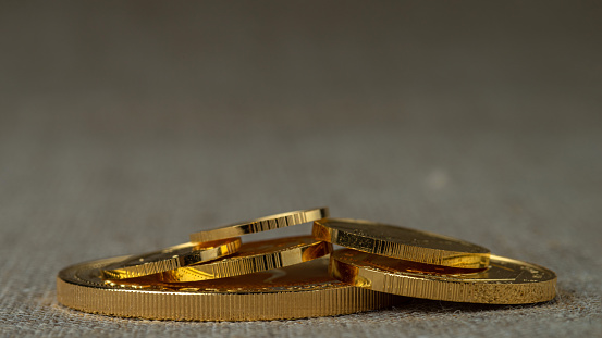A pile of gold coins of various sizes on a neutral blurred background. Selective focus.