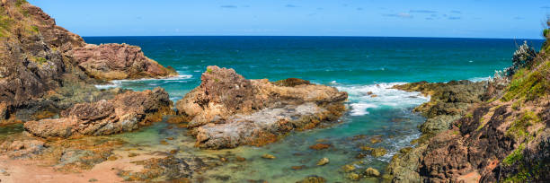 Australian coast with volcanic rocks in a small bay with blue water, seaside landscape, view from a cliff on a summer sunny day.