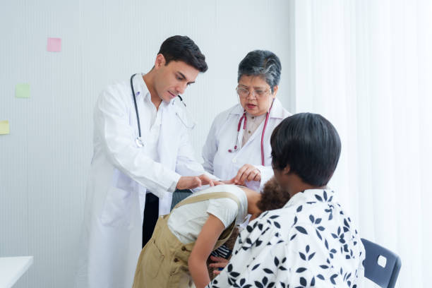 istock Medical assistant use stethoscope listen doctor touch back American child patient, is holding teddy bear in arms, tense as meets doctor in examination room, where doctor is checking for abnormalities. 1982933274