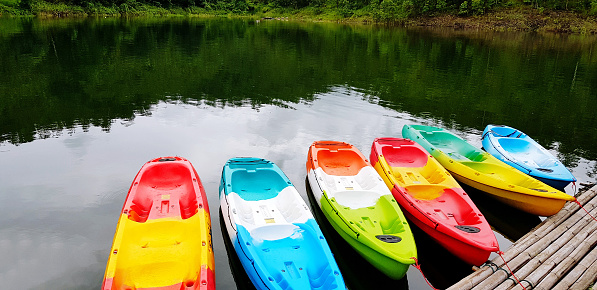 Many colorful canoeing or kayak boat parked on tropical lake with reflection for tourist and customers rent them with copy space at Amadard resort, Srinagarind Dam lake, Kanchanaburi, Thailand.