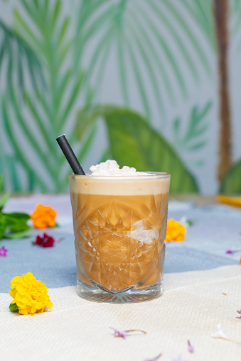 A cup of iced coffee latte with flowers in the backdrop on a table.