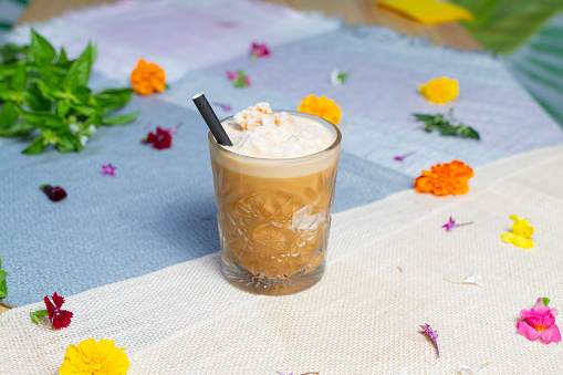 A cup of iced coffee latte with flowers in the backdrop on a table.