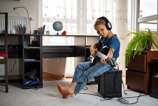 Little boy learning to play electric guitar. The boy is wearing a blue jeans t-shirt and blue jeans trousers. He is sitting on a large black amp and he is very focused on strumming the black guitar.
Shot with Nikon D800