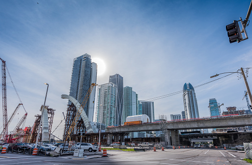 Miami, USA - February 1, 2024: View of live traffic next to cranes and heavy machinery next to new uninstalled parts of the new viaduct being built near downtown Miami (Project I-395/SR 836/I-95), where new luxury housing complexes are being developed.